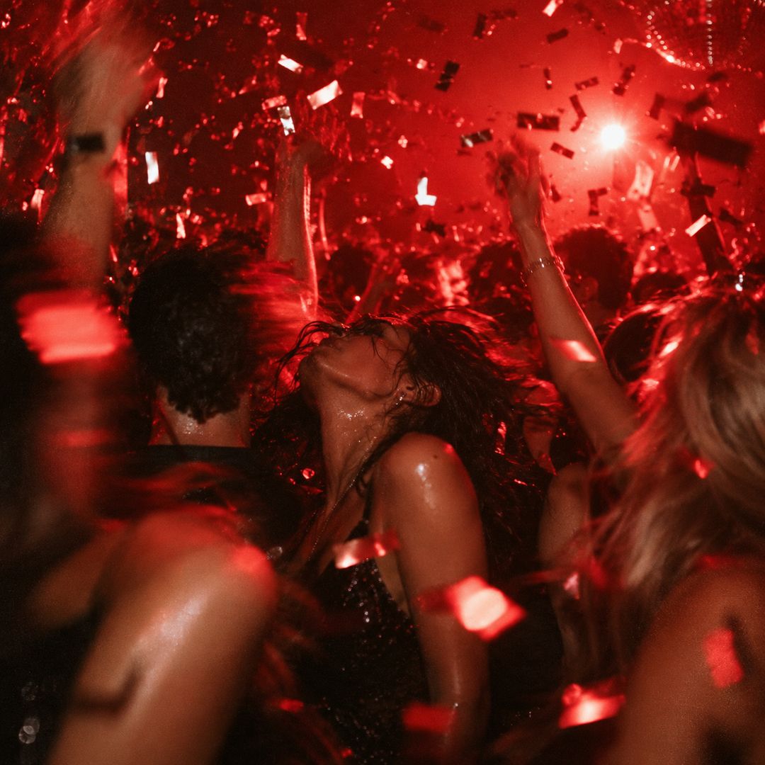 Crowd dancing under red light and confetti